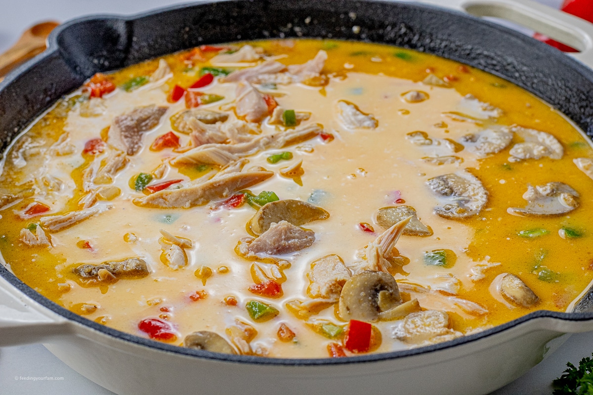 mushrooms, red, green peppers and chicken in a chicken broth mixture in a cast iron pan
