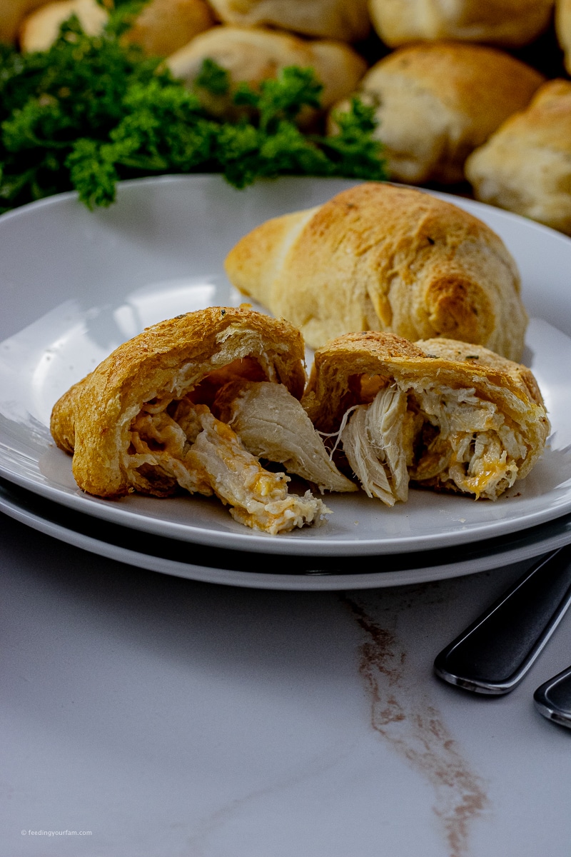 shredded chicken stuffed into a crescent roll that has been baked and broken in half on a white plate