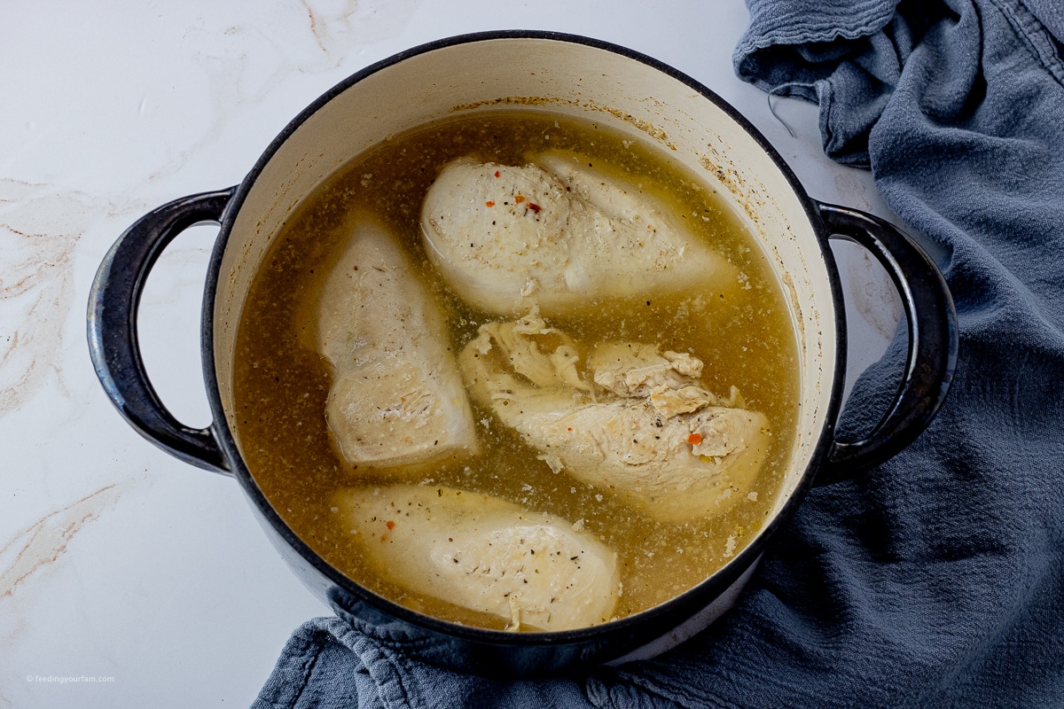 4 chicken breasts cooking in seasoned water in a large pot