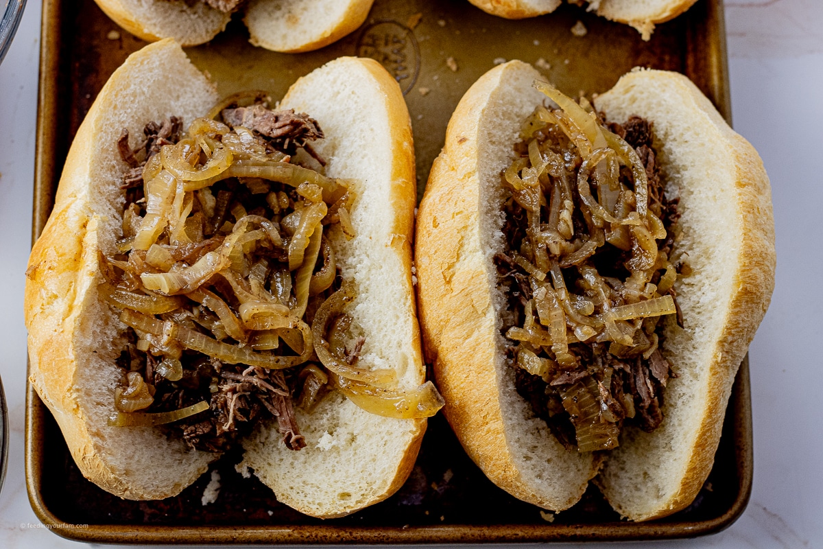 shredded beef topped with cooked onions in cut hoagie buns