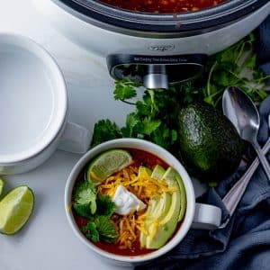 bowl of taco soup topped with avocado, sour cream, cheese and lime