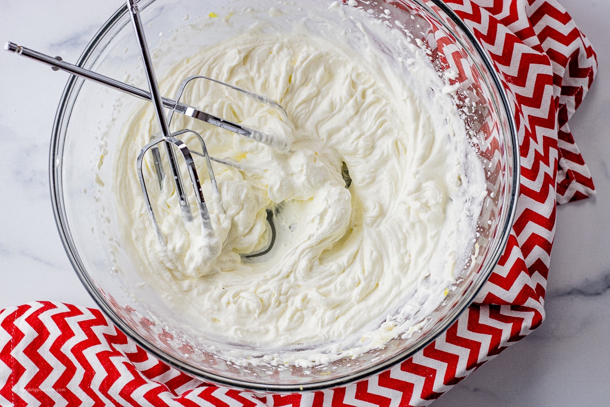 glass mixing bowl filled with lemon flavored whipped cream with two beaters in the bowl