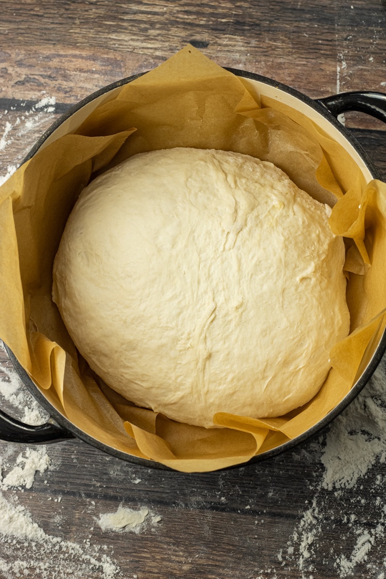 uncooked loaf of bread in a dutch oven pot lined with parchment paper