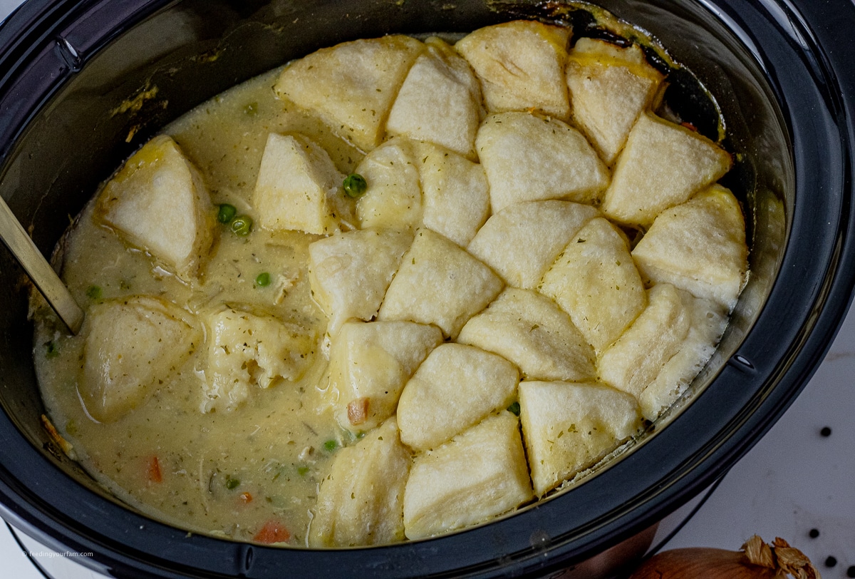 slow cooker pot filled with chicken and dumpling soup, topped with biscuits