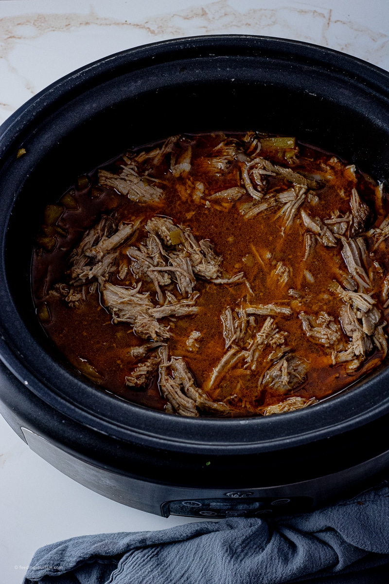 shredded pork in a slow cooker with all the juices it was cooked in