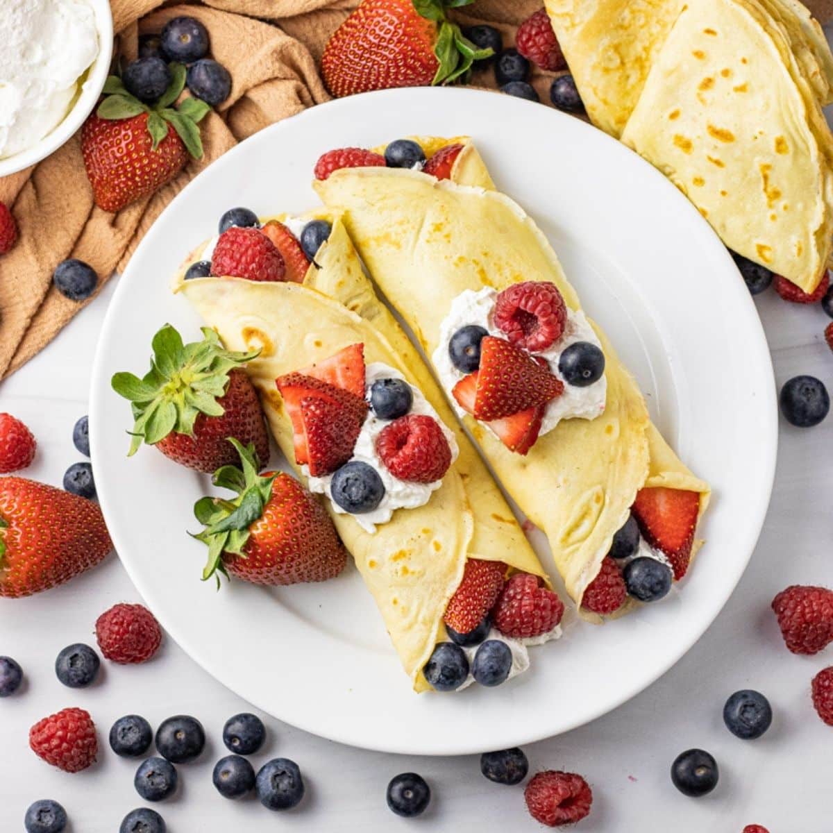 crepes filled with fruit and whipped cream rolled up on a white plate