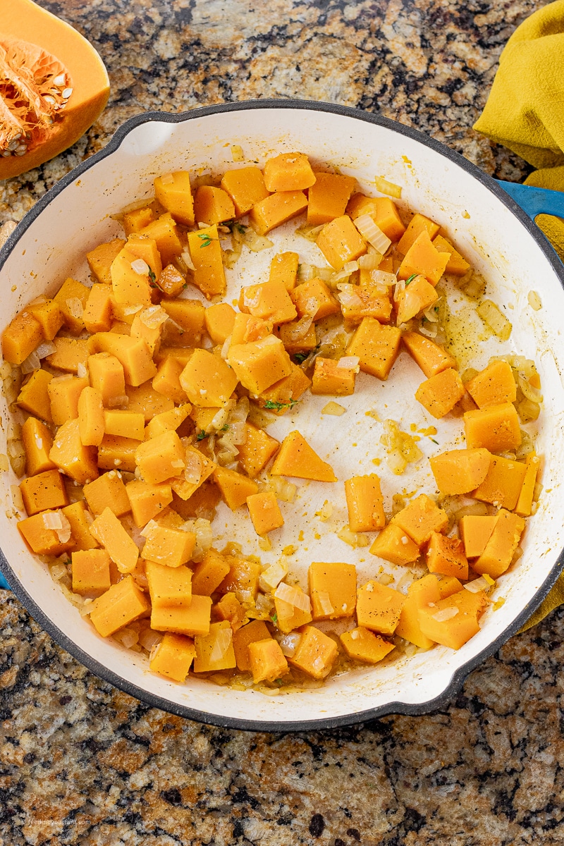 pieces of butternut squash in a large pan cooked with onions and garlic
