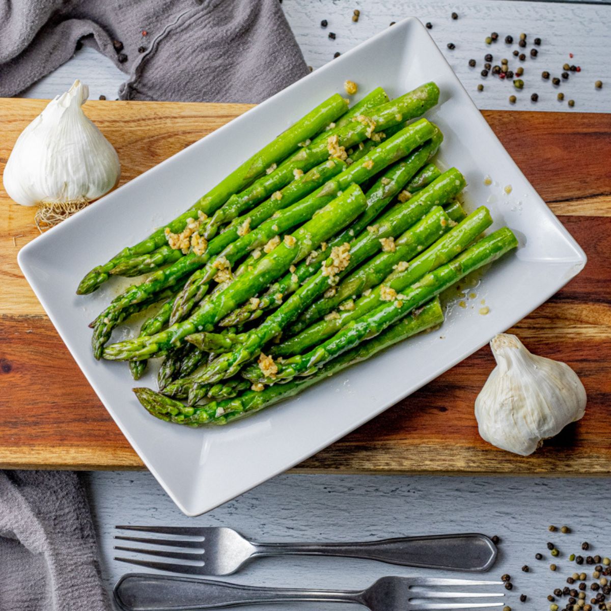 asparagus topped with butter and garlic on a white platter