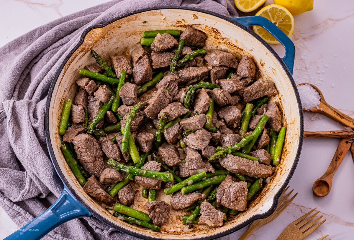 a cast iron pan filled with garlic and butter steak bites with pieces of asparagus