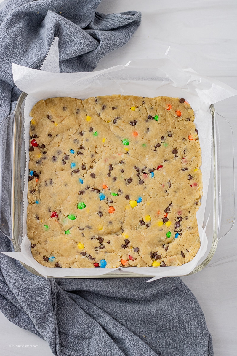 uncooked chocolate chip cookie dough bars with mini chocolate candy pieces pressed into a square baking pan 