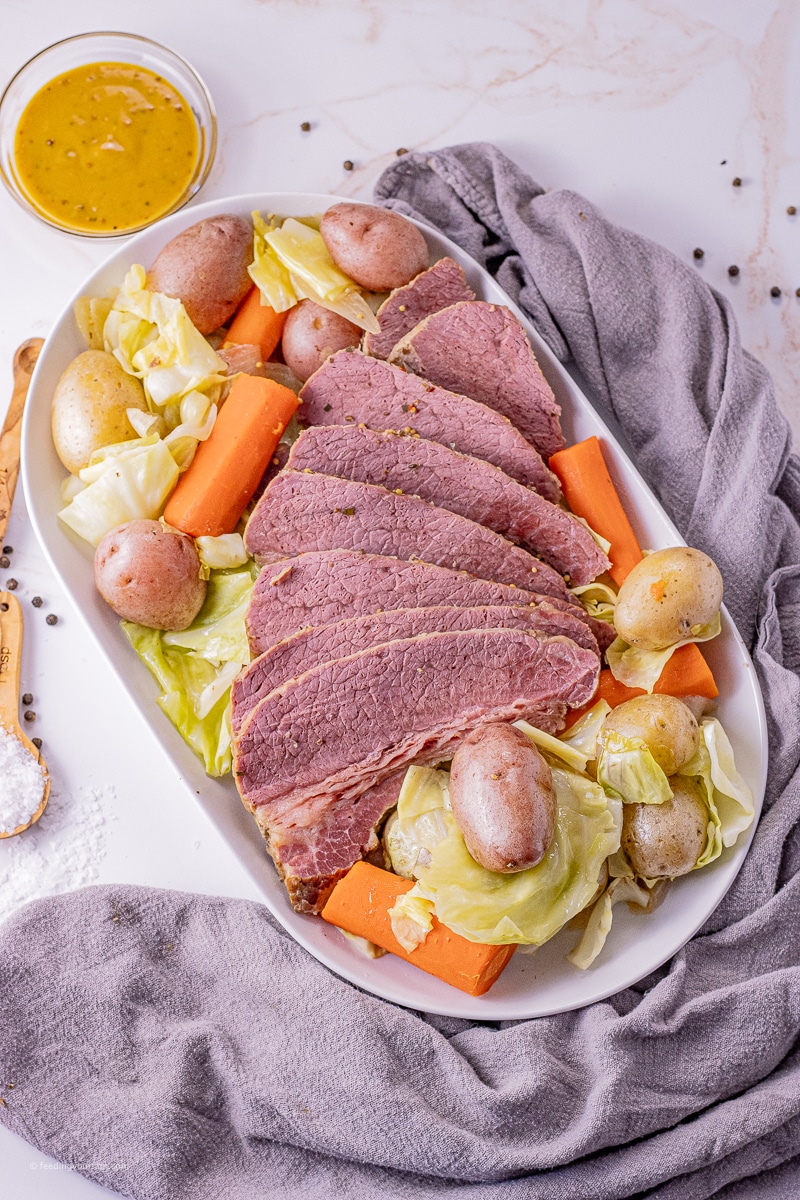 sliced corned beef on a white platter with potatoes, carrots, and cabbage
