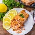 cast iron cooked salmon on a white plate with lemon slices