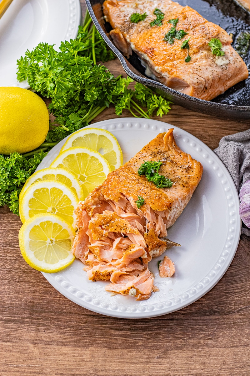 cast iron cooked salmon on a white plate with the salmon flaked a little bit with some lemon slices