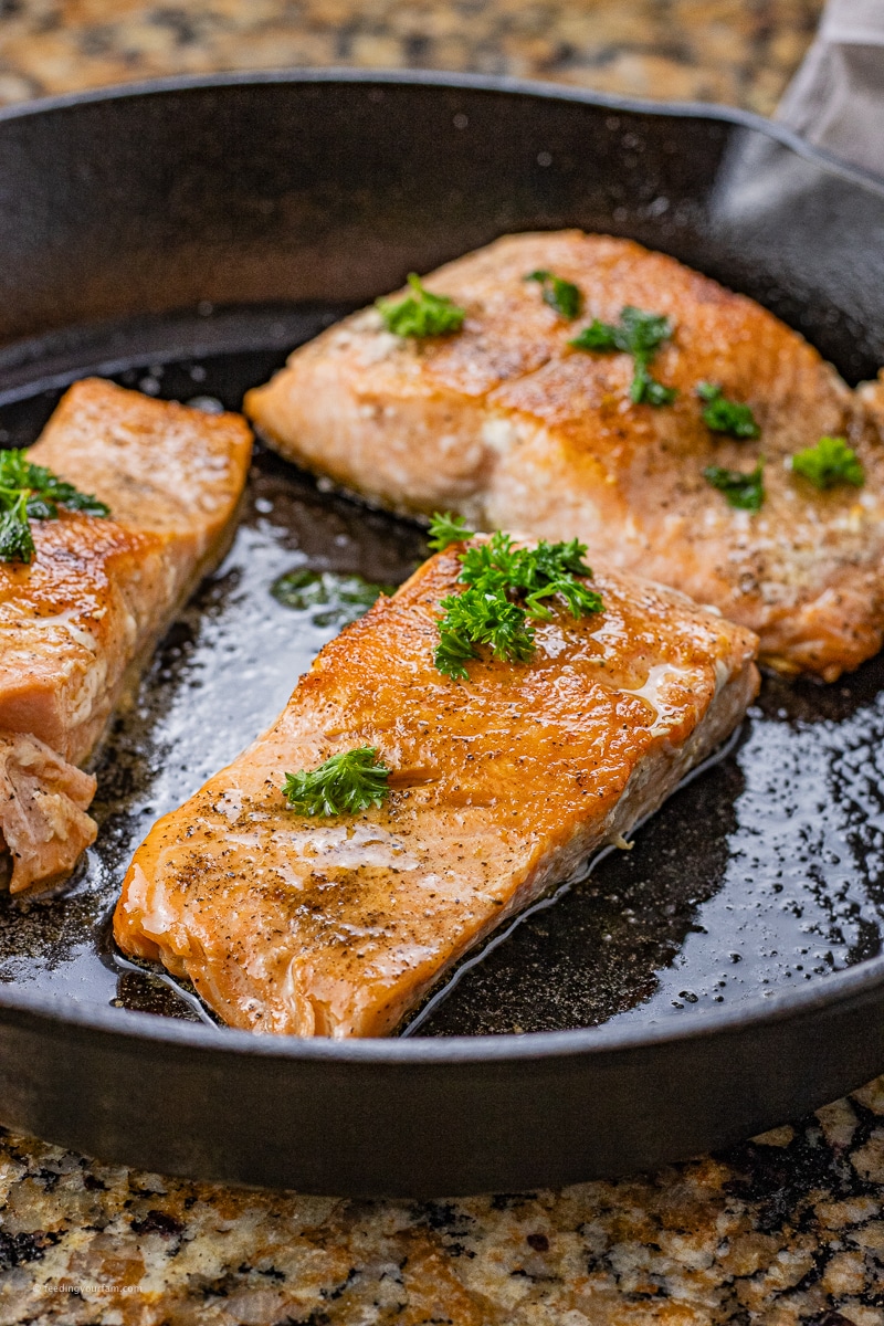 salmon filets in a cast iron pan topped with parsley and melted butter