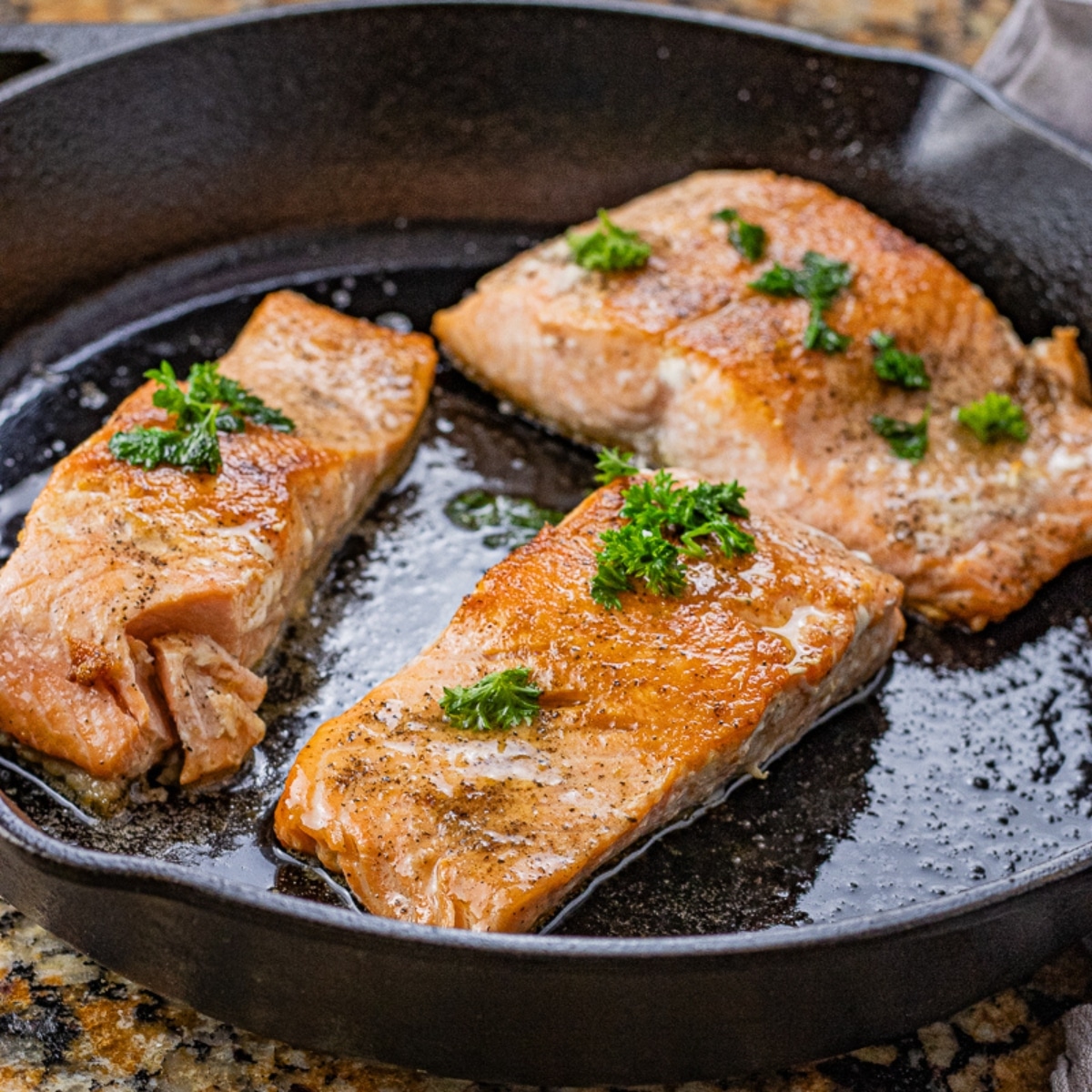 three salmon filets cooked in a cast iron pan