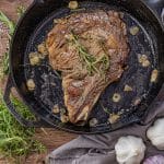 ribeye steak cooked in a cast iron pan with thyme, rosemary and sliced garlic