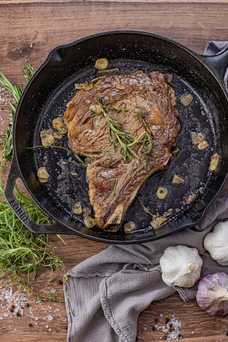 ribeye steak cooked in a cast iron pan with thyme, rosemary and sliced garlic