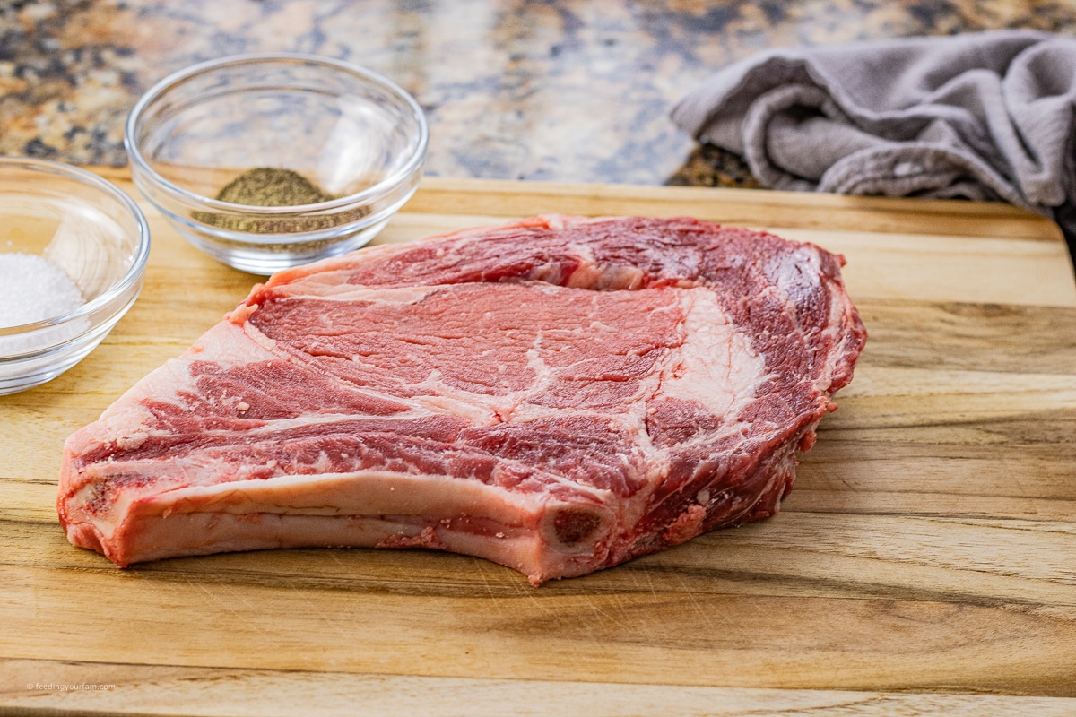uncooked ribeye steak on a wooden cutting board
