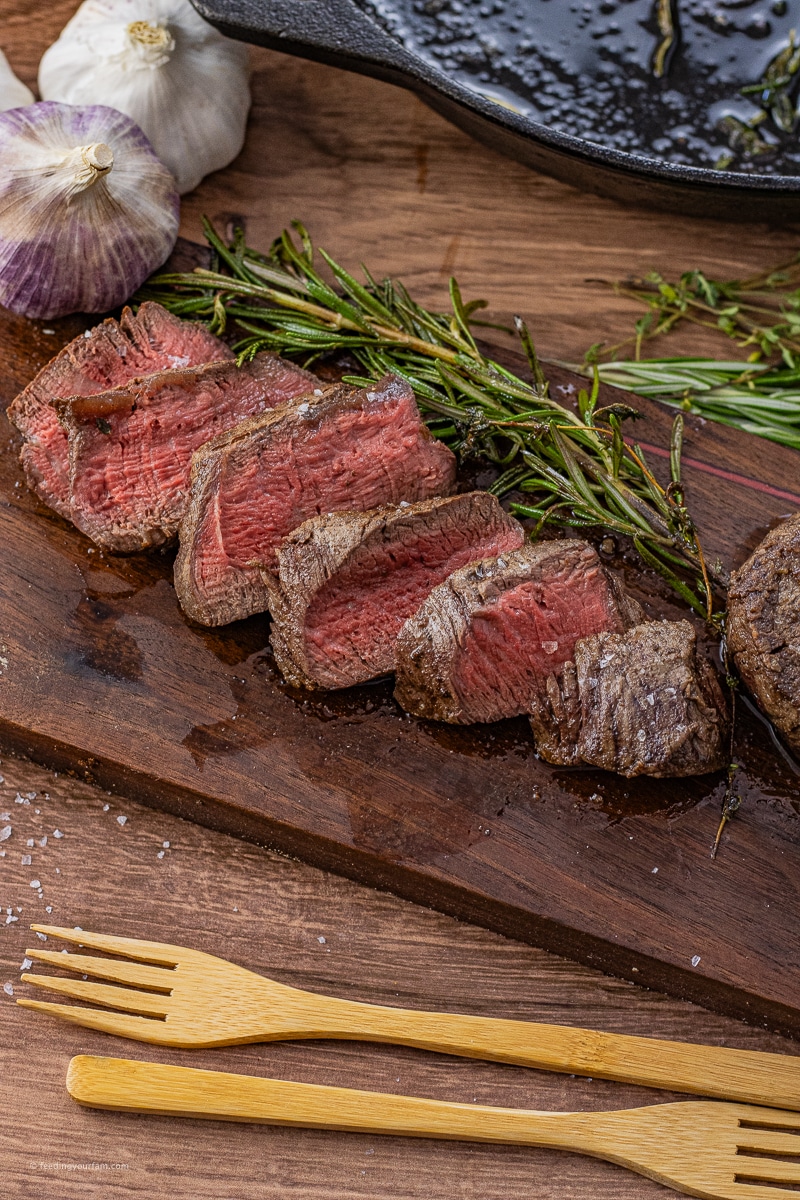 sliced filet mignon on a wooden cutting board with rosemary sprigs
