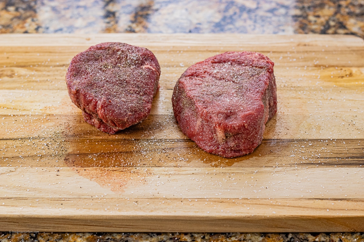 two uncooked filet mignons seasoned with salt and black pepper