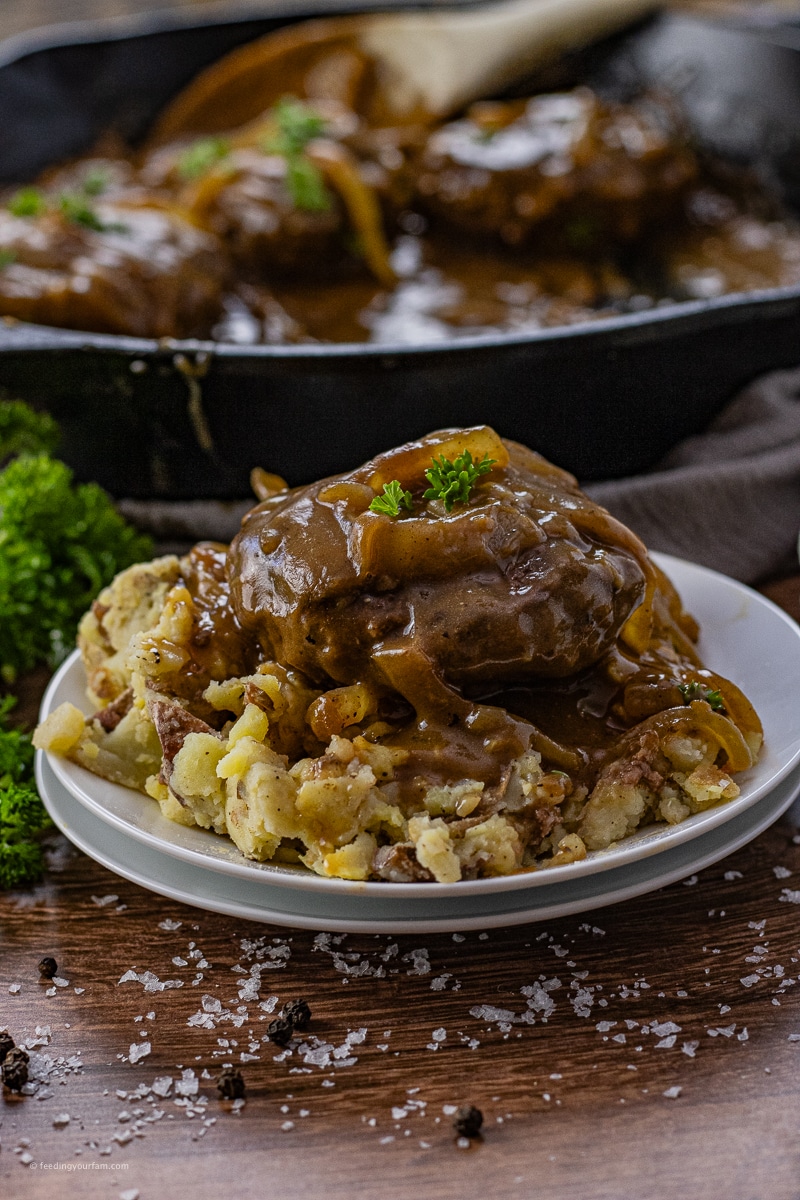 onion gravy hamburger steaks over mashed potatoes on a round, white plate