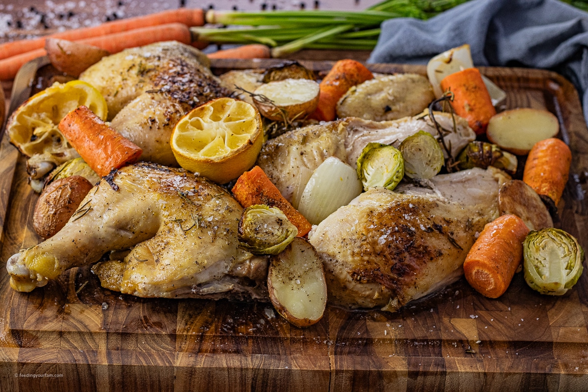 sliced roasted chicken with vegetables on a wooden cutting board.