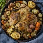 whole chicken in a cast iron skillet with potatoes, carrots and brussels sprouts baked around it