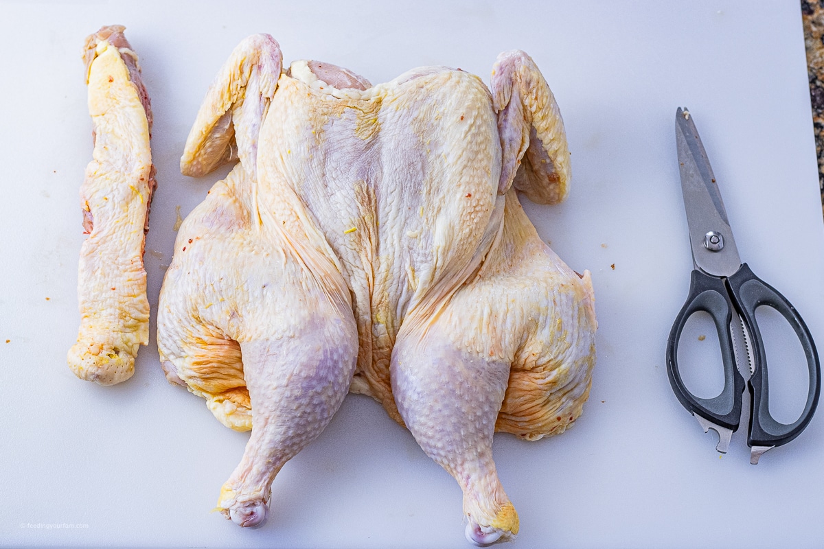 spatchcock raw chicken on a white cutting board