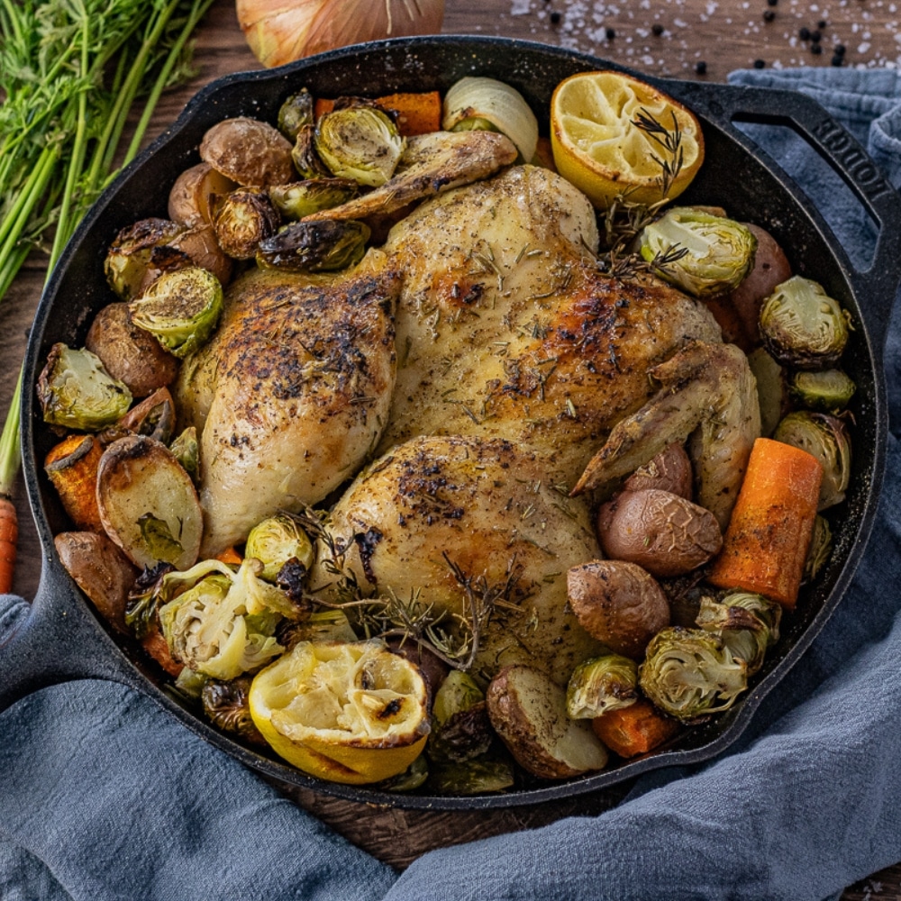 roast chicken in a cast iron skillet with vegetables around it