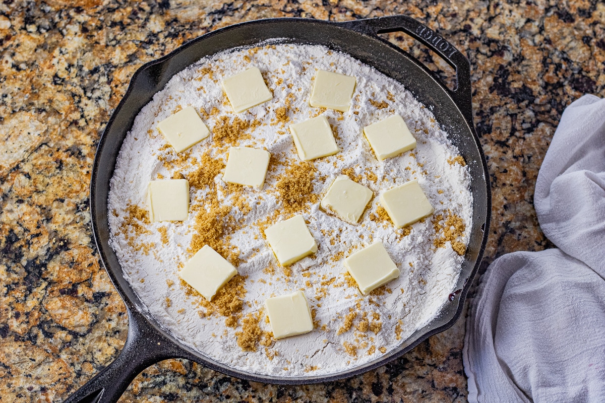 uncooked cherry pineapple dump cake topped with butter slices in a cast iron skillet