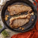 two new york steaks cooked in a cast iron skillet with garlic and thyme sprigs