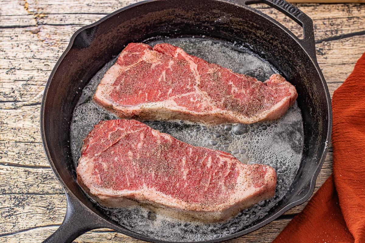 new york strip steaks cooking in a cast iron skillet in butter