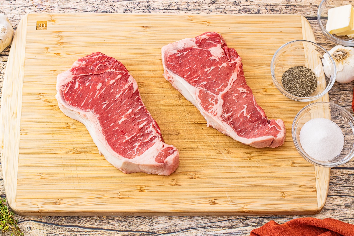 uncooked new york steaks on a wooden cutting board