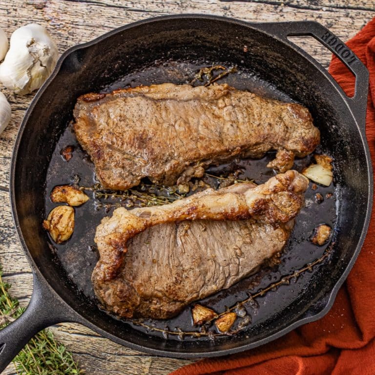 2 new york steaks cooked in a cast iron skillet with garlic and thyme leaves