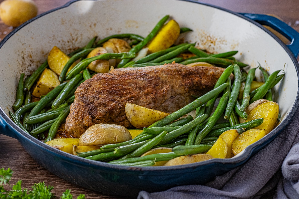 pork tenderloin cooked in a cast iron pan with golden potatoes and green beans