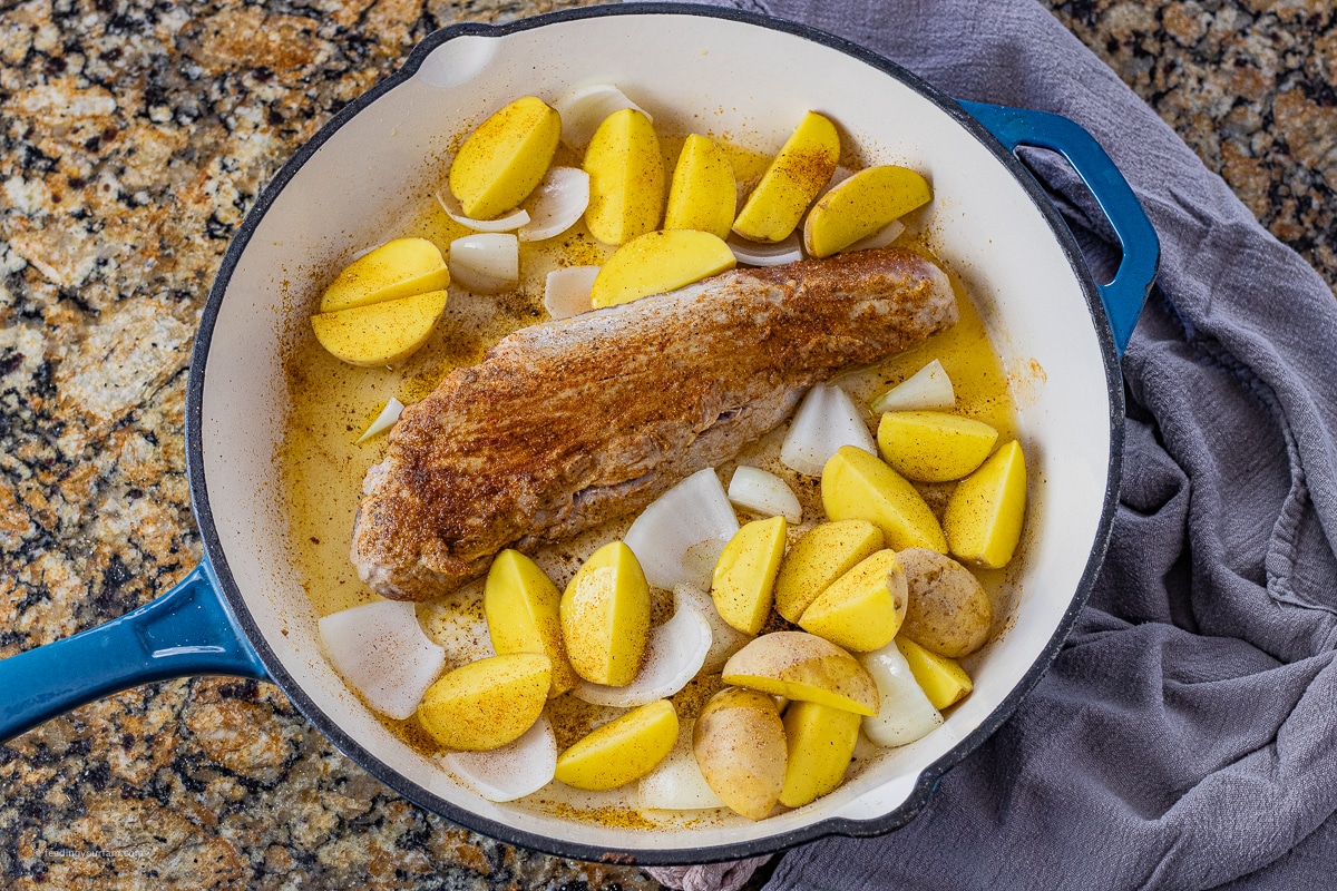 browned pork tenderloin in a cast iron pan with golden potatoes and sliced onions