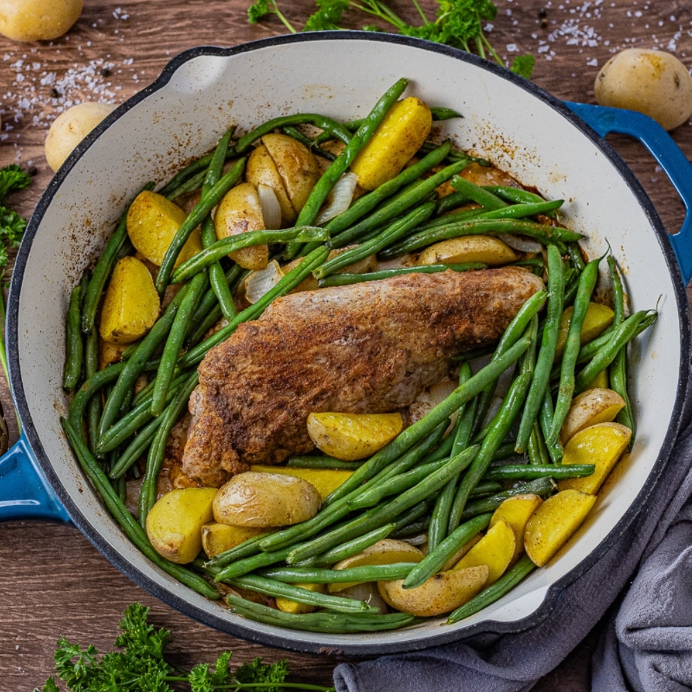 oven cooked pork tenderloin in a cast iron pan with green beans and golden potatoes.