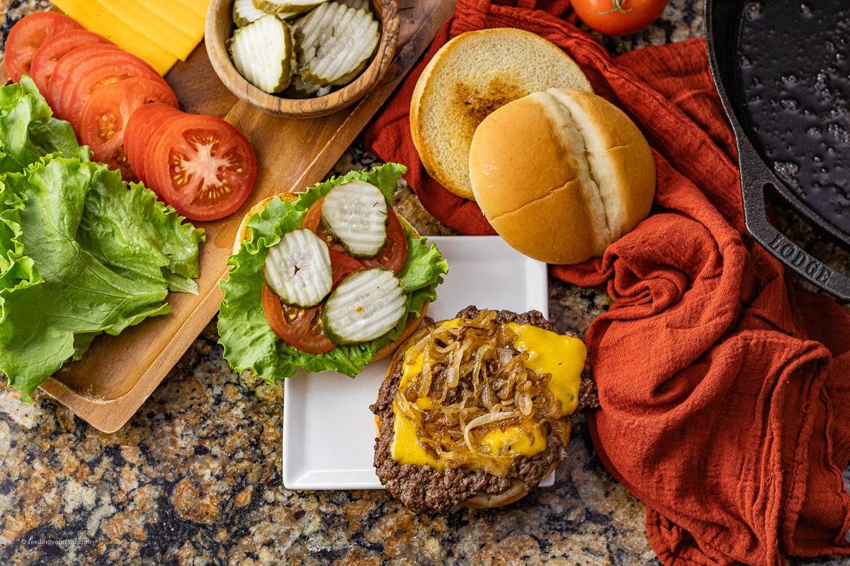 cheeseburger topped with caramelized onions on a bun with pickles, tomatoes and lettuce