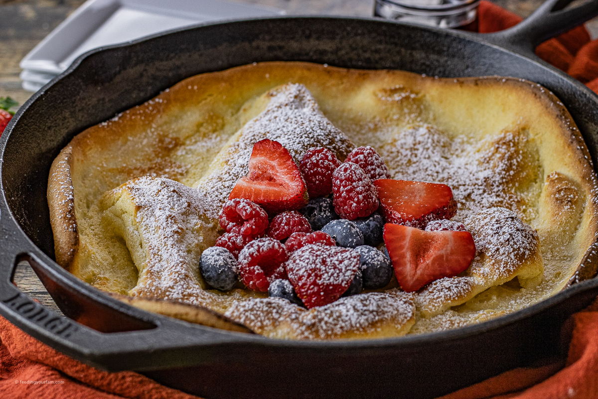 dutch baby pancake topped with fresh berries and powdered sugar