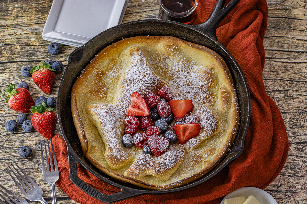 cast iron skillet with a dutch baby pancake baked inside with fruit and powdered sugar on top of it