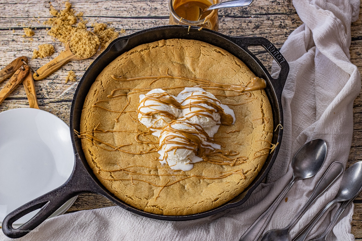 peanut butter cookie in a cast iron skillet topped with vanilla ice cream and a drizzle of peanut butter