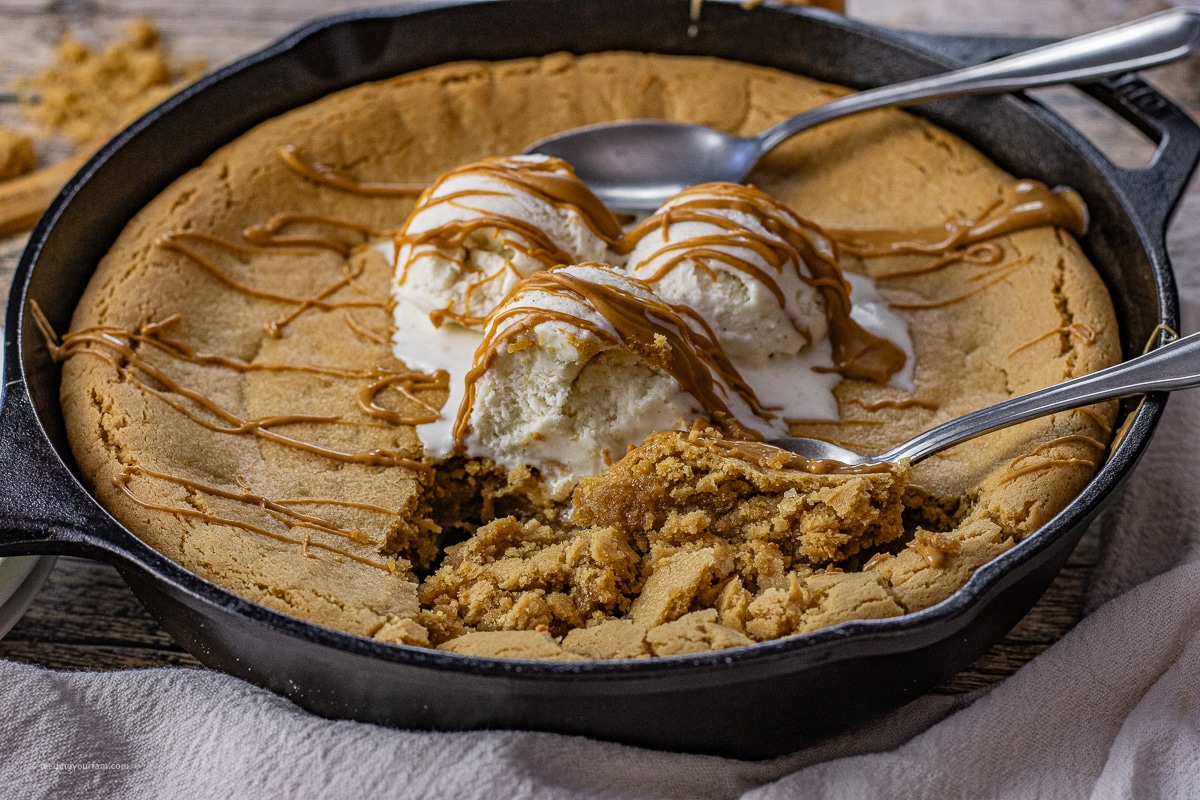 giant peanut butter pizookie cooked in a cast iron skillet topped with vanila ice cream scoops 