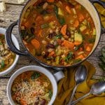 big pot of minestrone soup with two smaller bowls of soup next to it