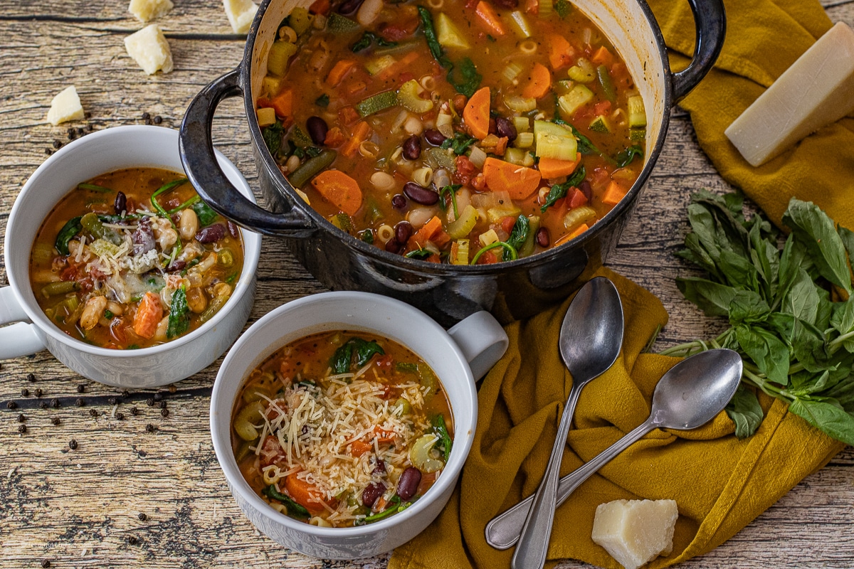 minestrone soup in a big pot with two smaller bowls of soup next to it