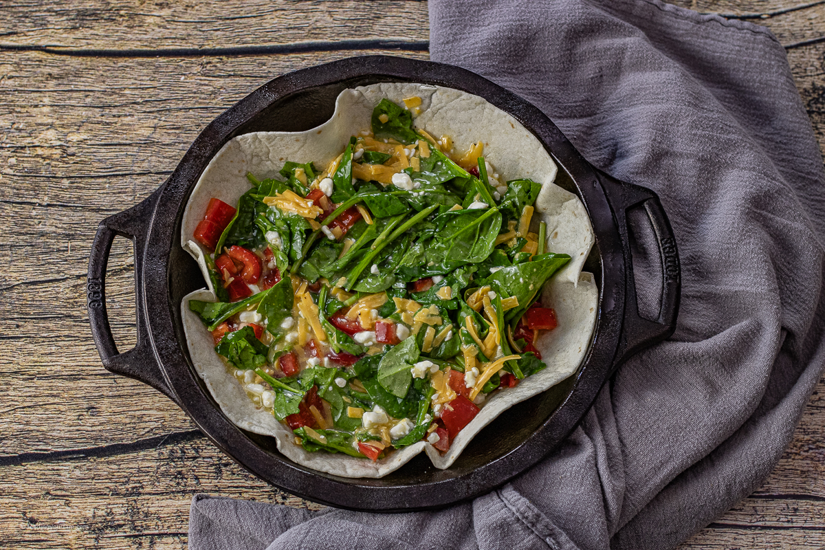 uncooked tortilla egg bake with spinach, cottage cheese, cheddar cheese and eggs in a pie pan