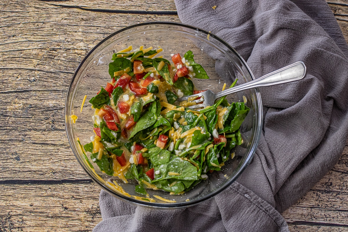 spinach, red peppers, cheddar cheese, cottage cheese and eggs all mixed together in a glass mixing bowl