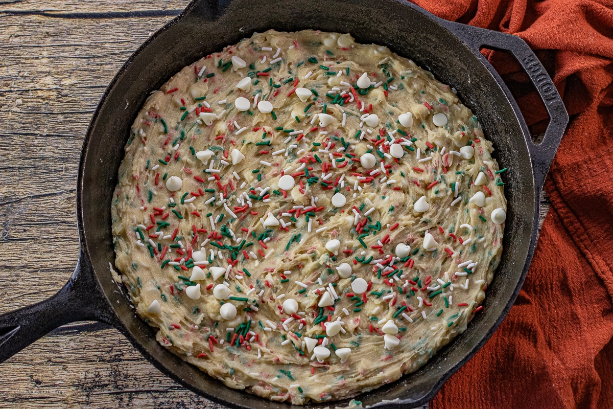 uncooked cookie dough with red and green sprinkles in a cast iron skillet