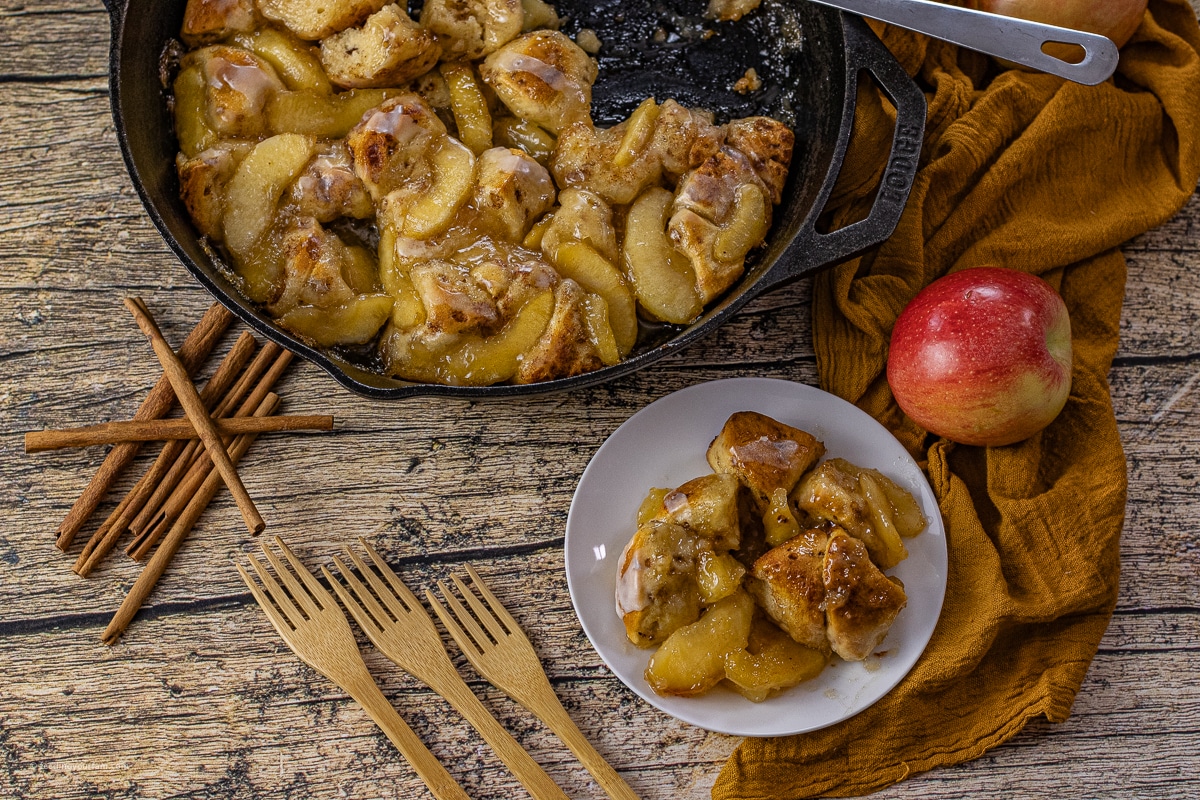 apple pie filling with cinnamon rolls baked in a cast iron skillet, some is on a white, round plate