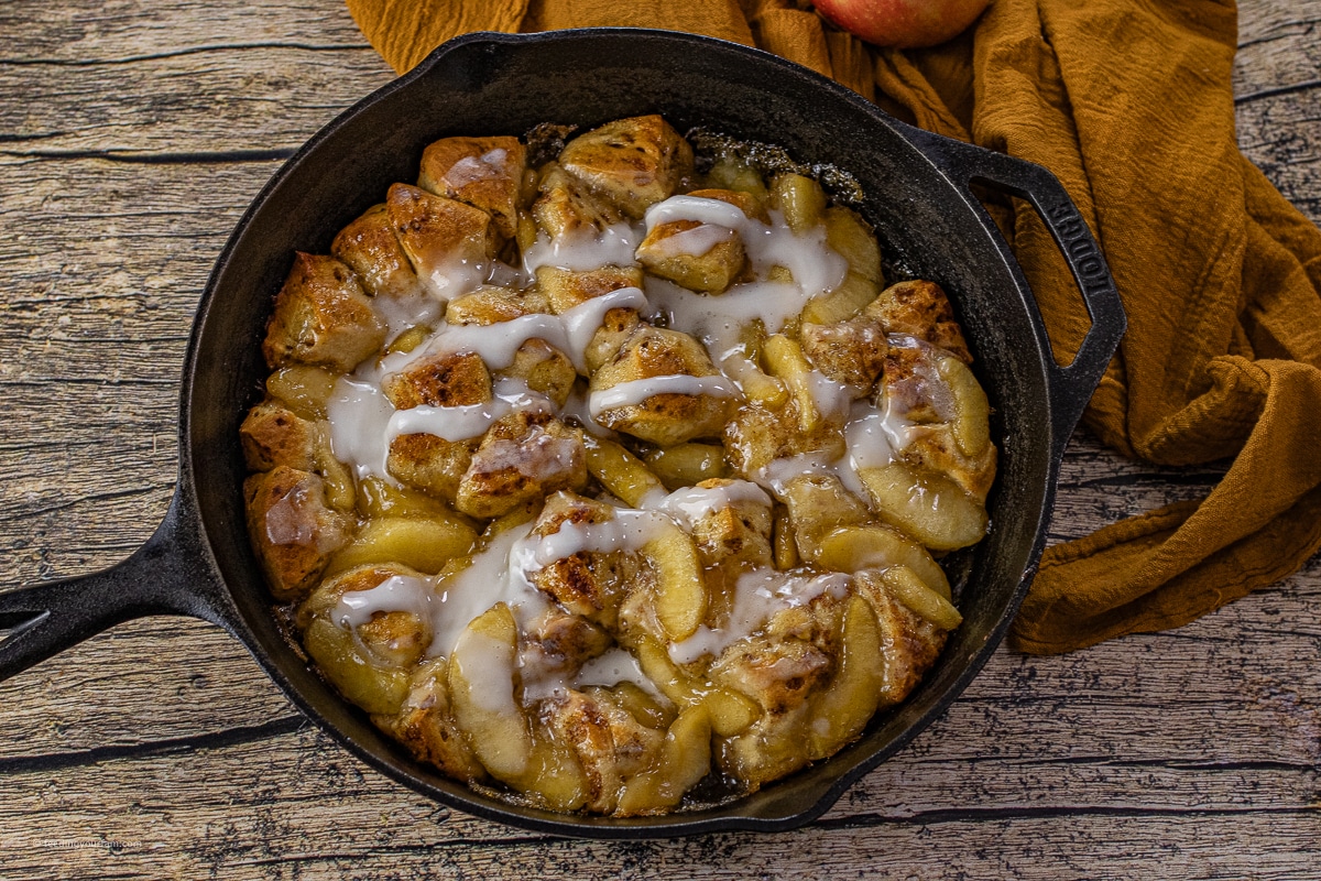 cast iron skillet with baked cinnamon rolls and apple pie filling 