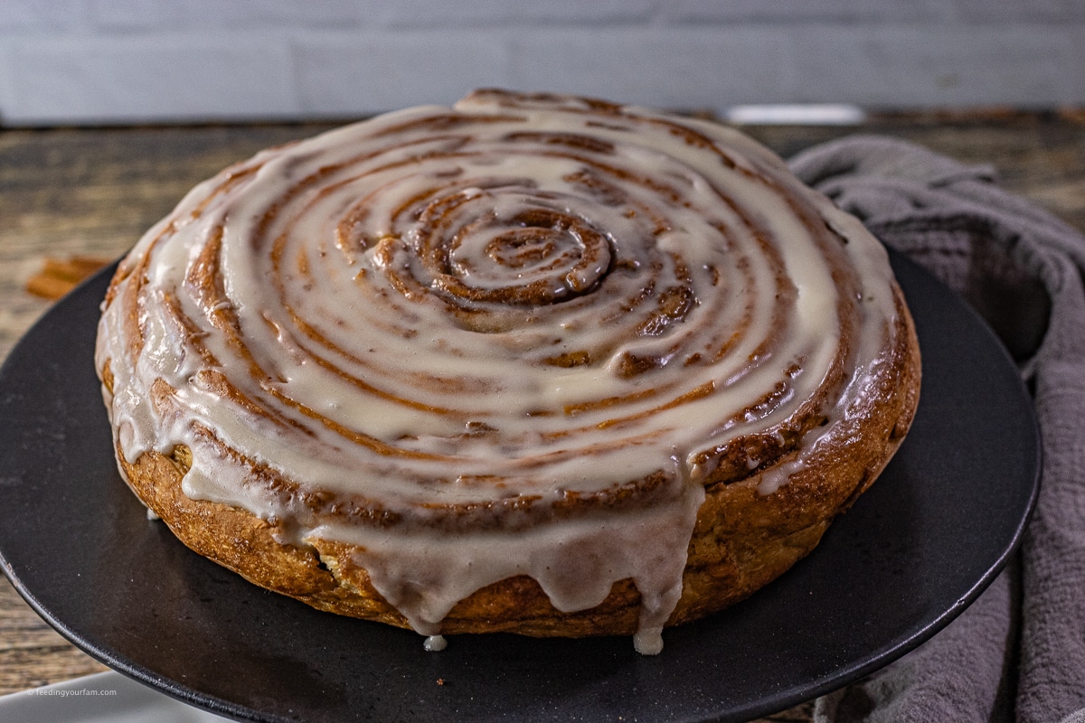 giant cinnamon toll with frosting on a black plate